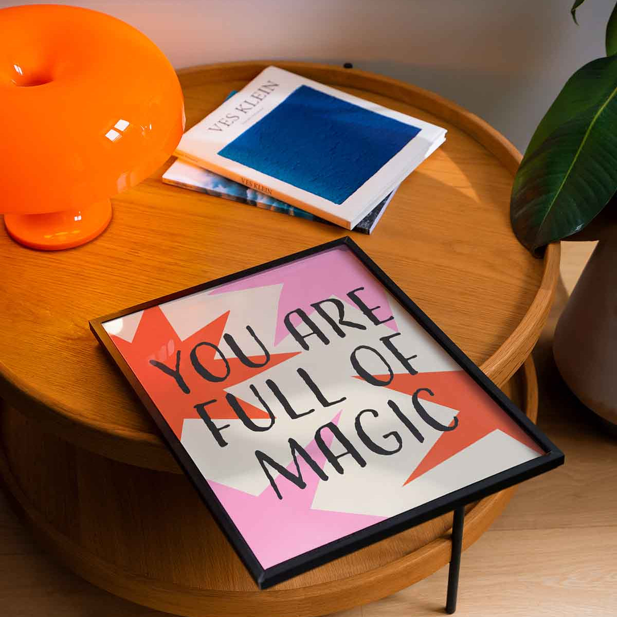 Decorative sign with 'You are full of magic' on a wooden table with a lamp and books.
